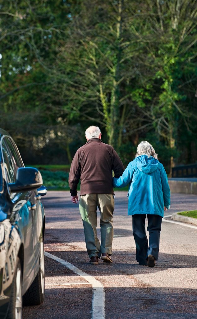 Elderly couple walking down a path holding hands.